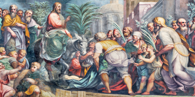 Jesus entering Jerusalem with people putting blankets down and welcoming him with palms.